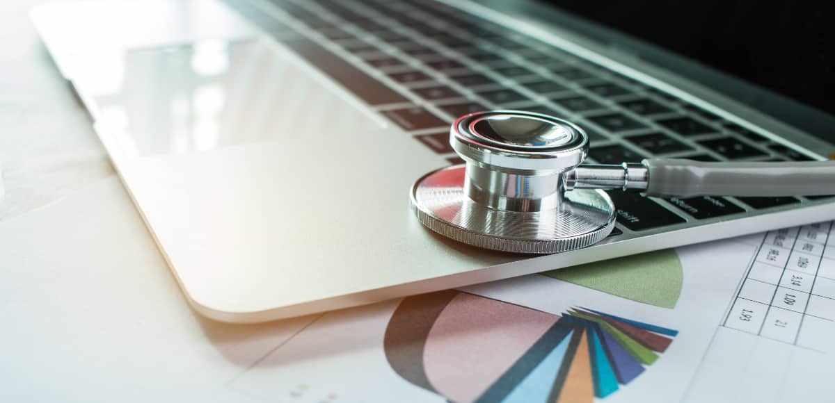 A stethoscope sitting on top of an open laptop computer and a printed pie chart