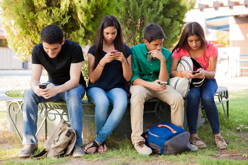The Elephant In The Room: How To Talk To Teens About Sex Group of teens sitting outside using cell phones and not talking to each other