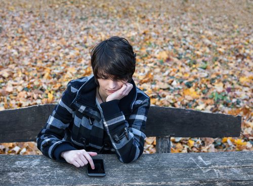 The Elephant In The Room: How To Talk To Teens About Sex Lonely teen girl on cell phone sitting on bench.